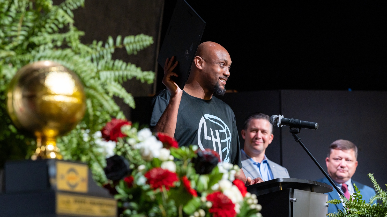Coach Trenton Hassell smiling and holding the coach of the year award with 2 men in background